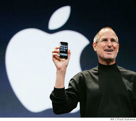 Steve Jobs con l’iPhone in piedi davanti al logo Apple